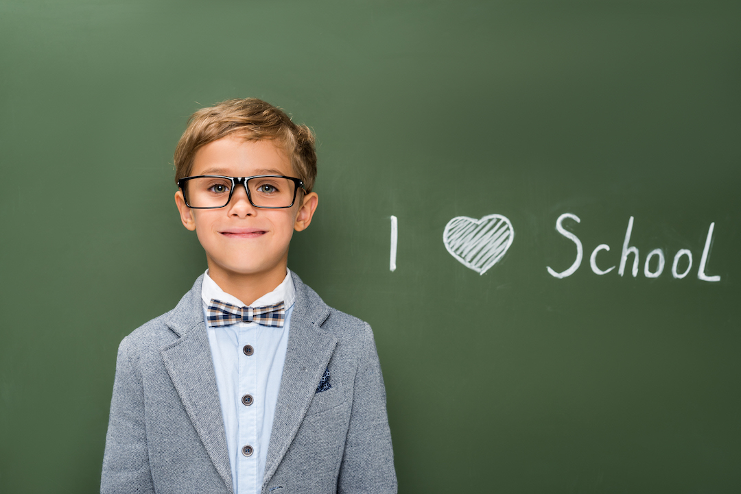 smiling schoolboy in eyeglasses next to chalkboard with i love school sign