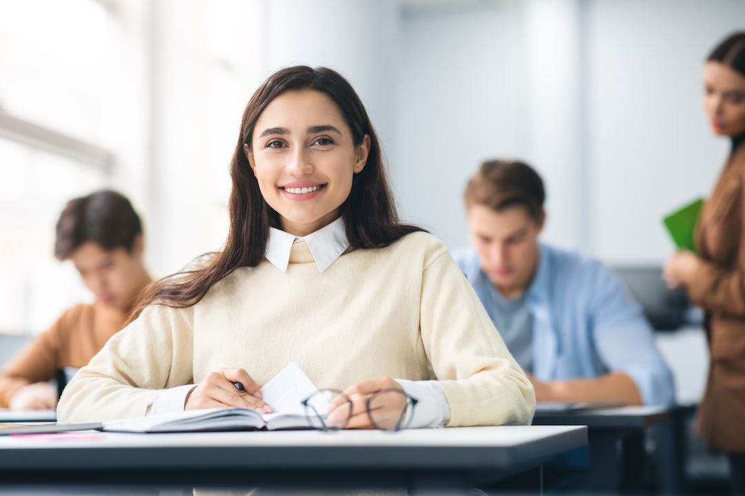 Smiling student sitting at desk in classroom posing at camera