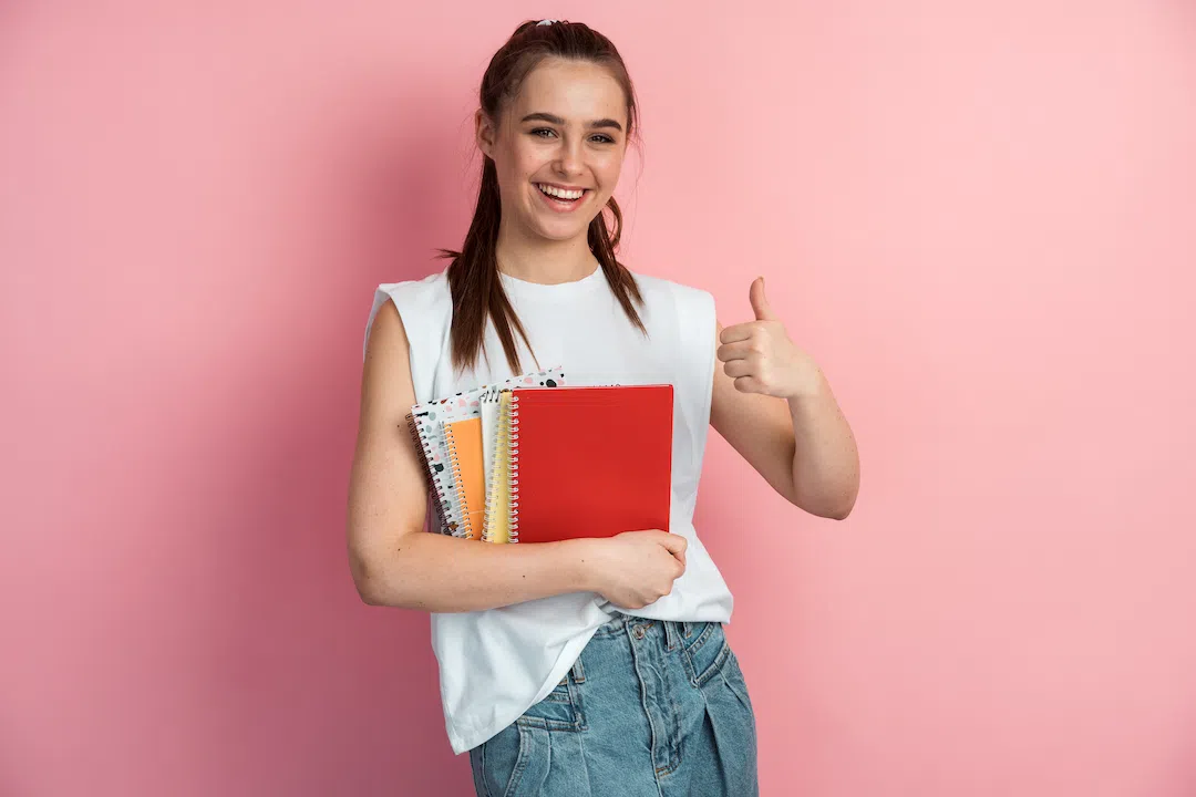 cute-positive-girl-with-books-in-her-hands-shows-2022-01-06-17-34-12-utc