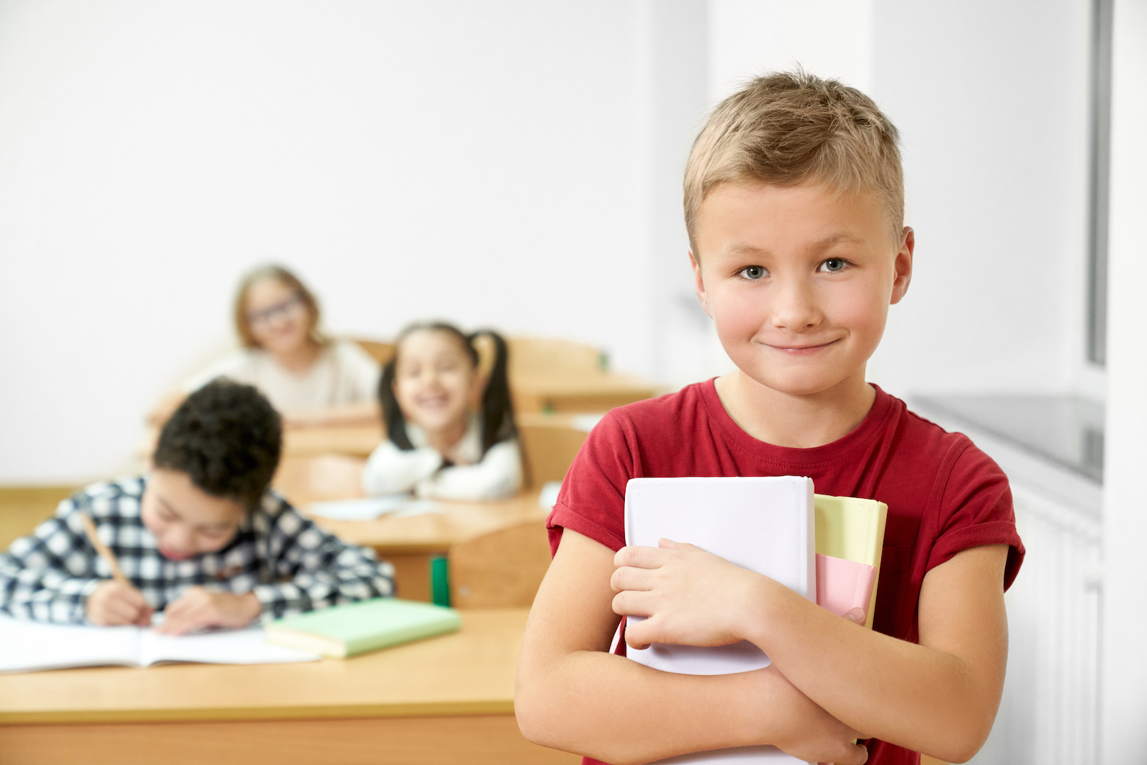 Schoolboy holding books, looking at camera, smiling.